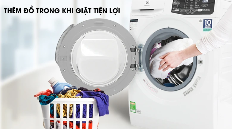 Máy giặt Electrolux EWF12025GWA với cửa trước mở, người dùng đang thêm đồ vào lồng giặt, bên cạnh là giỏ đựng quần áo.